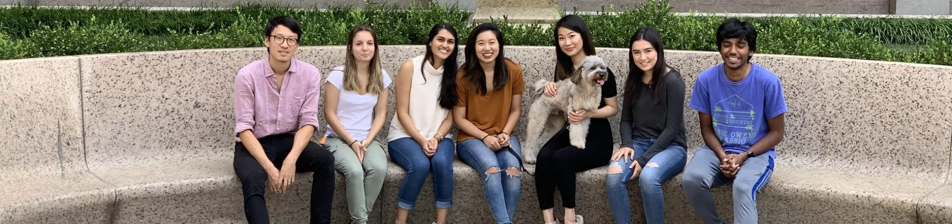 A group of seven students and a small dog sit on a concrete ledge in front of the Columbia Engineering and Computer Science building sign.