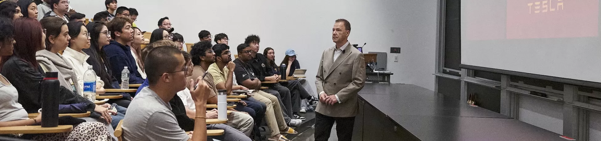 Attendees seated in an institutional room with accessibility-designated seating, watching or waiting during what appears to be a formal proceeding or meeting.
